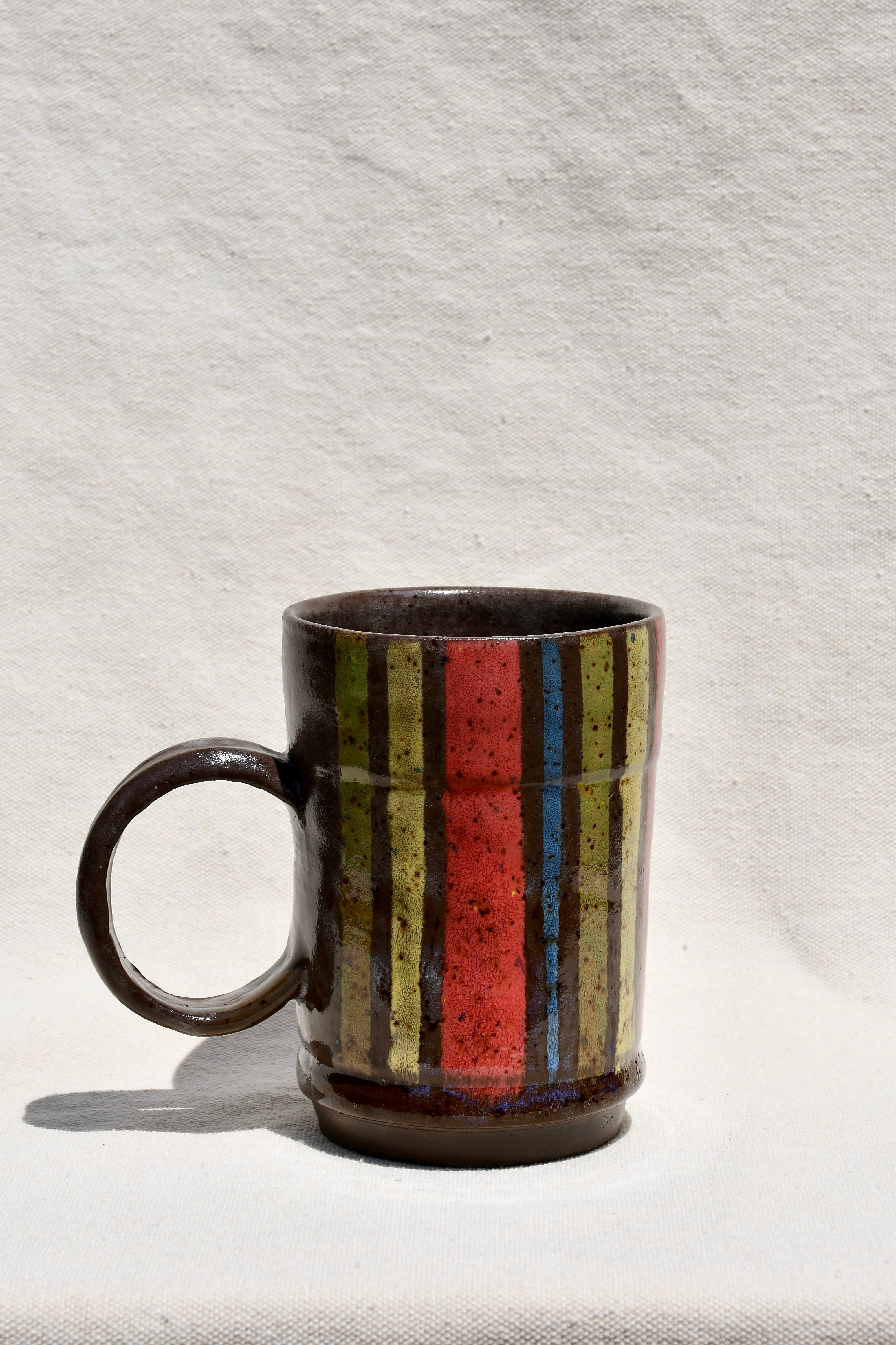 Yellow, Brown, Red, Green, Blue striped mug with round handle.