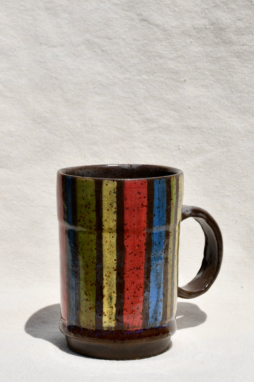 Yellow, Brown, Red, Green, Blue striped mug with round handle.