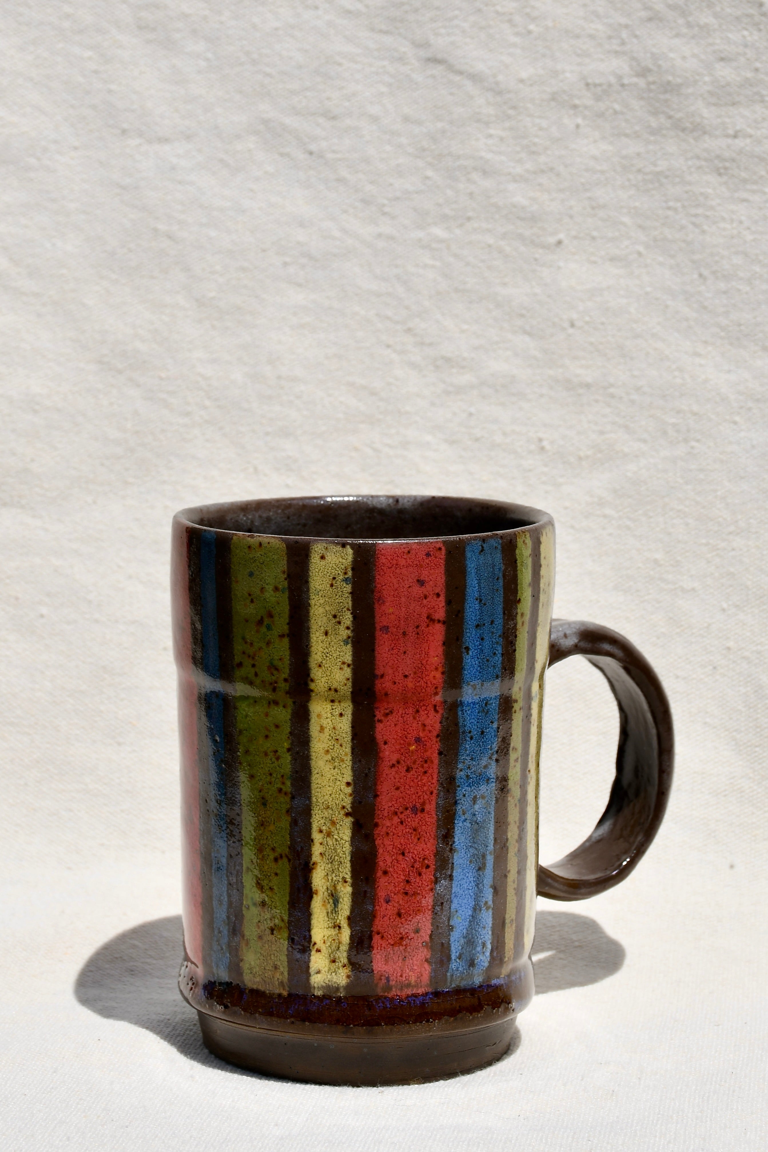 Yellow, Brown, Red, Green, Blue striped mug with round handle.