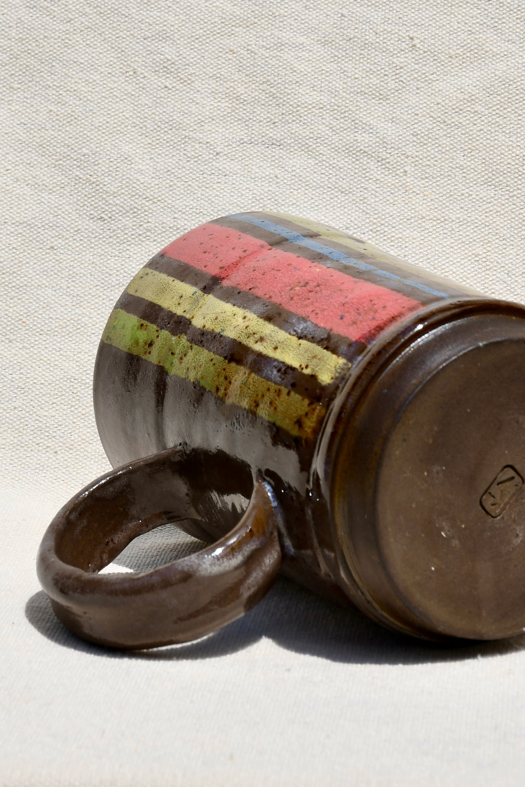 Yellow, Brown, Red, Green, Blue striped mug with round handle.