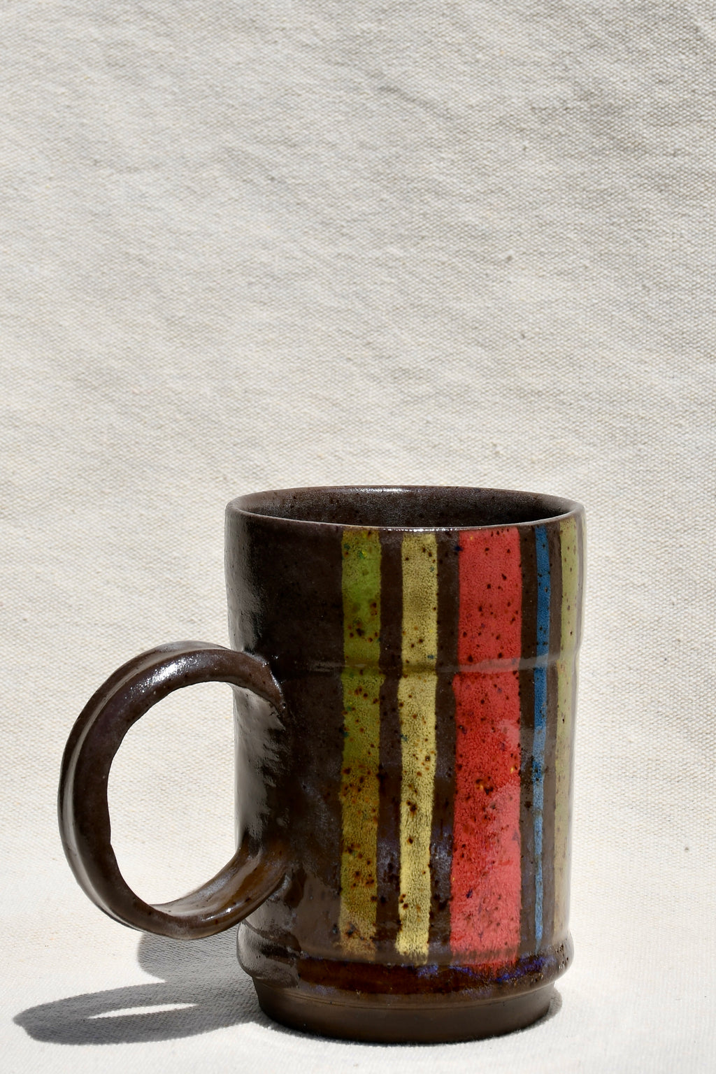 Yellow, Brown, Red, Green, Blue striped mug with round handle.