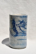 A handmade ceramic cylinder vase with a blue dragon design, featuring a speckled glaze and a textured, hand-painted finish, set against a white background with a soft shadow.